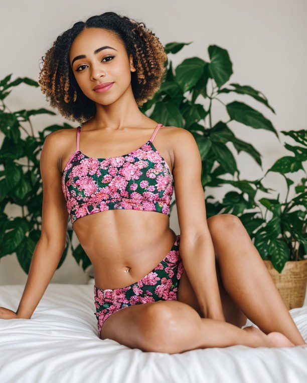 Vinfluencer Zuri Ames in pink floral activewear surrounded by greenery on a white bed.