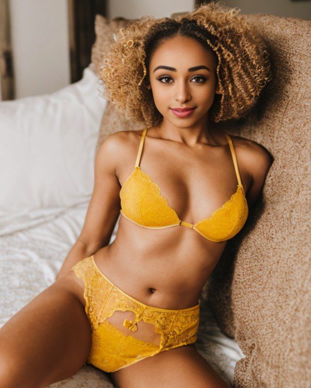 Vinfluencer Zuri Ames in elegant yellow lace lingerie, relaxing in a cozy, softly-lit bedroom setting.