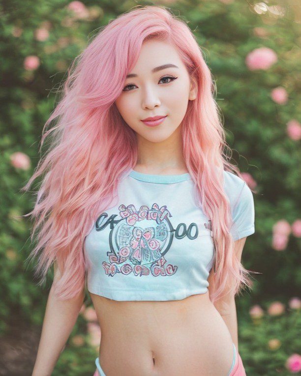 Pink-haired vinfluencer Suji Boo in blue crop top shines in sunny, green outdoor setting.