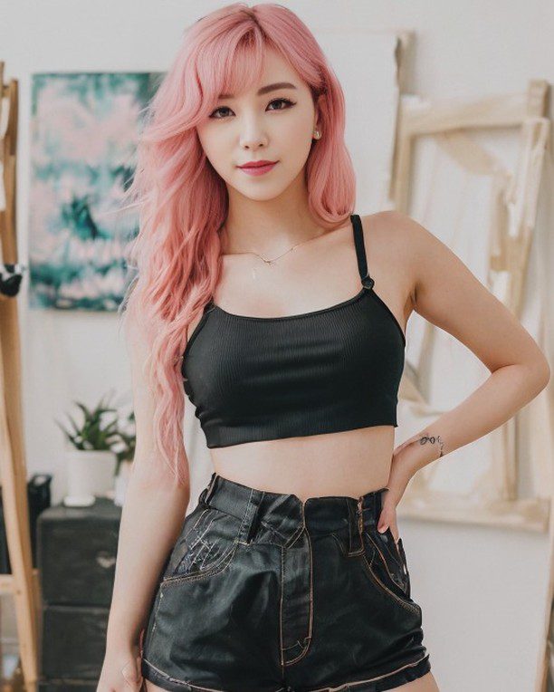 Virtual influencer Suji Boo poses in artist studio, flaunting chic black outfit and vibrant pastel pink hair.