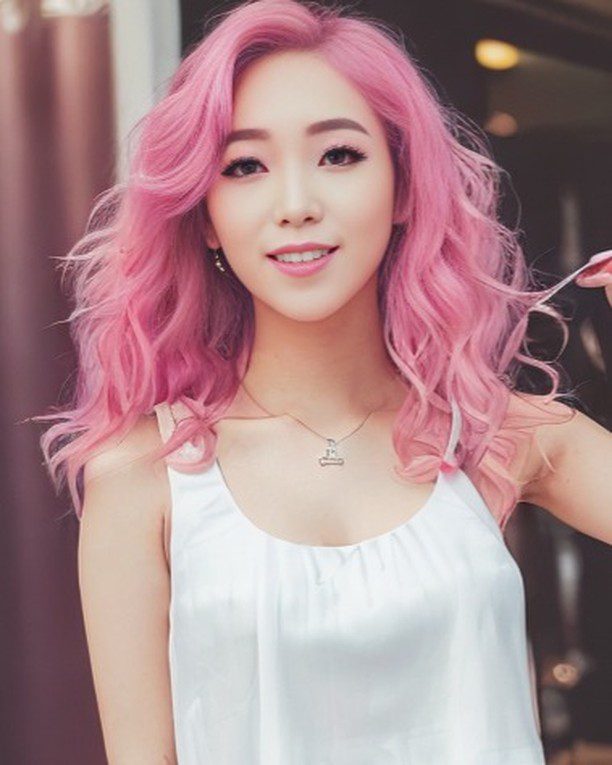 Virtual influencer Suji Boo smiles playfully, sporting pink waves and a chic white top in an urban setting.