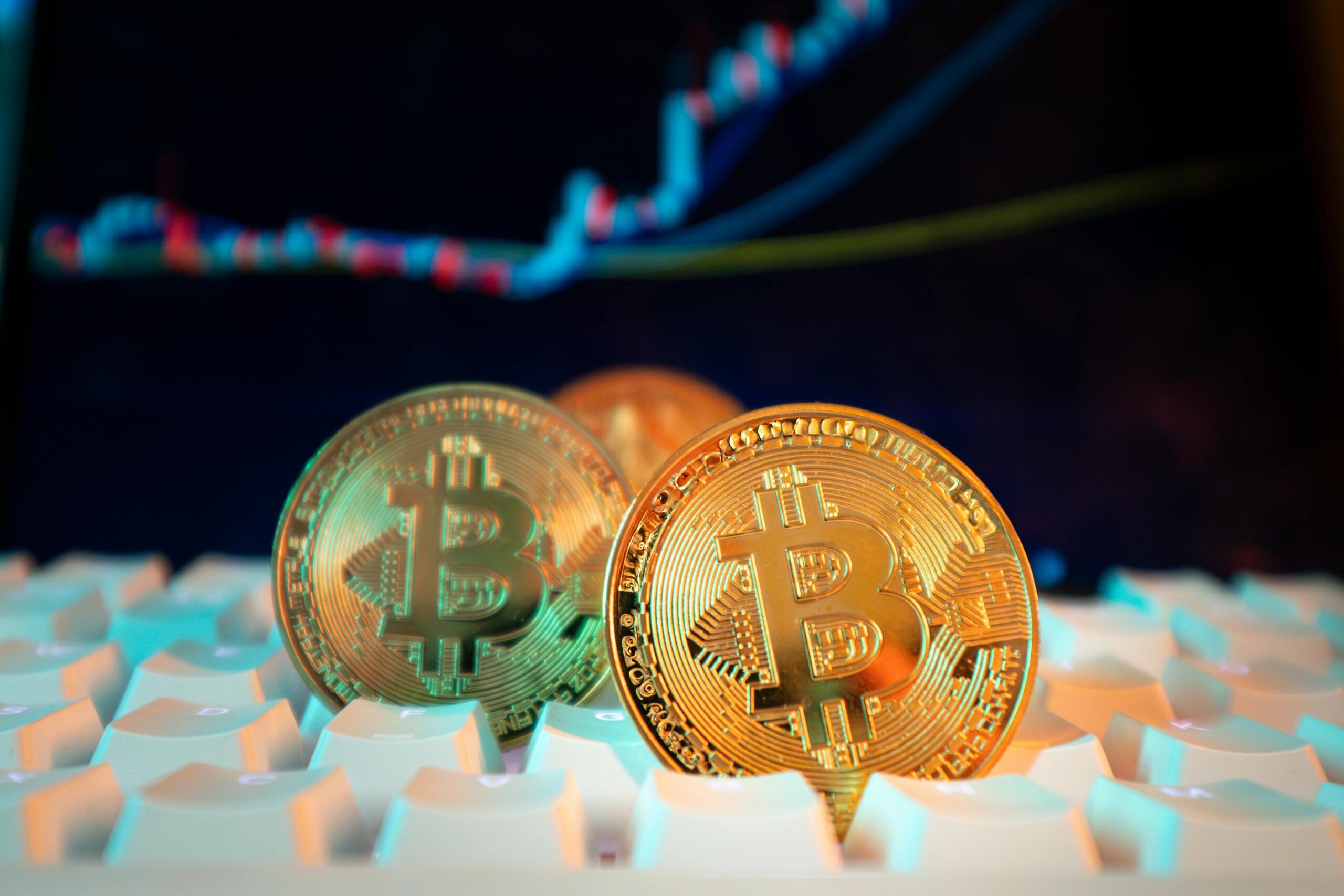A single Bitcoin coin resting on a dark keyboard, lit from one side, like an offering left on a desk