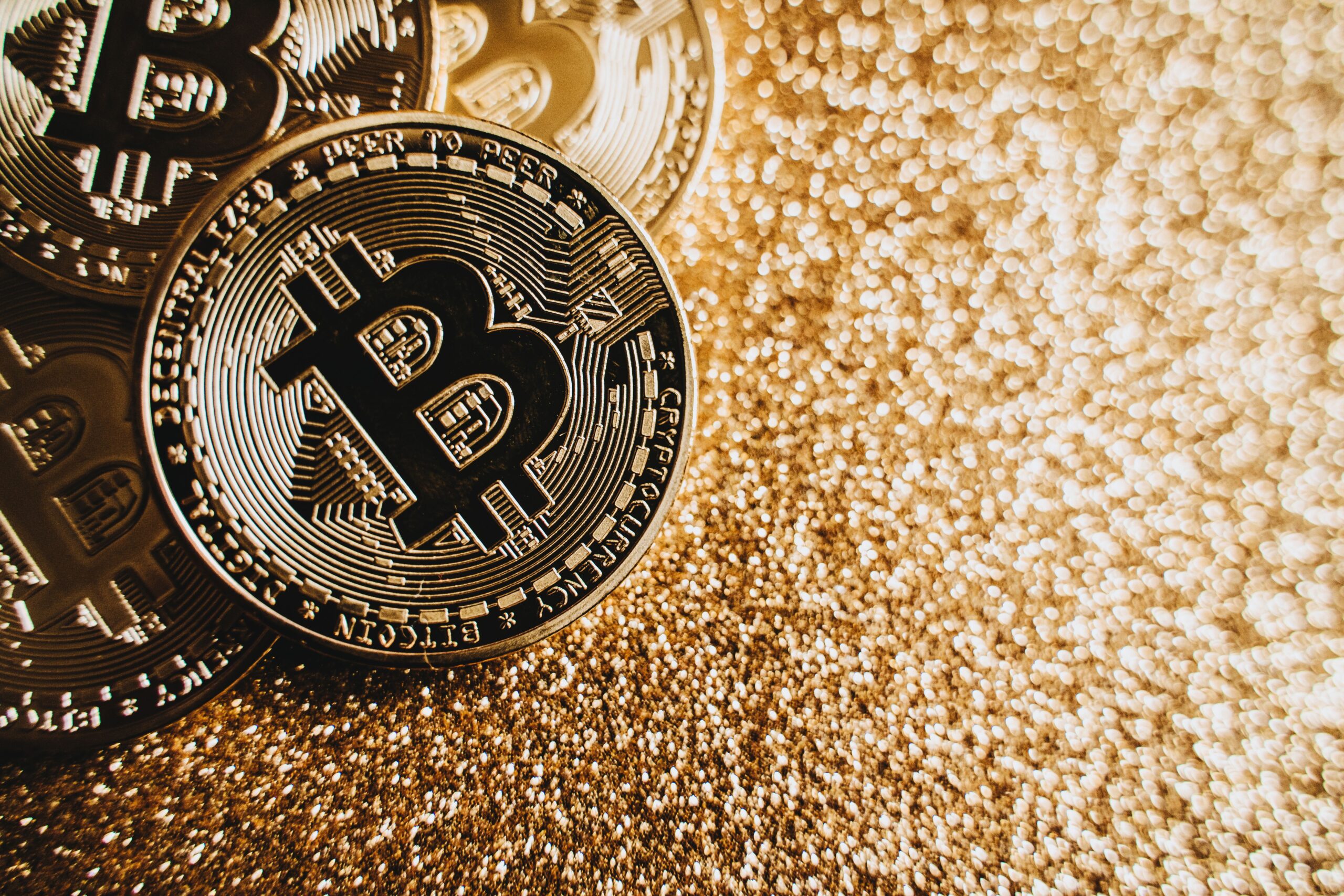 Bitcoin coins on a dark metallic surface lit from a single angle, evoking the closing of an era.