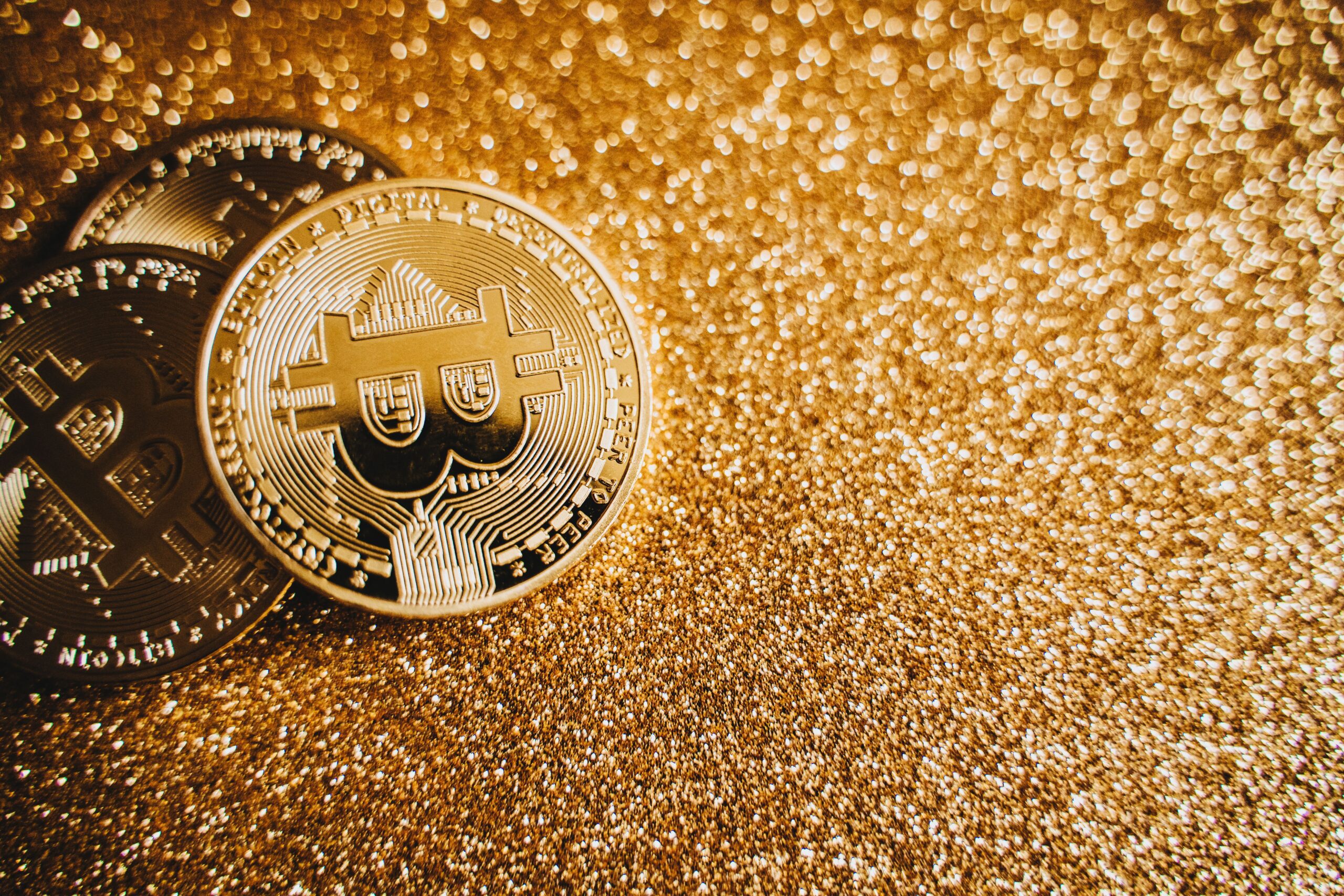 A single gold Bitcoin coin lit from one side on a dark surface, monumental and still
