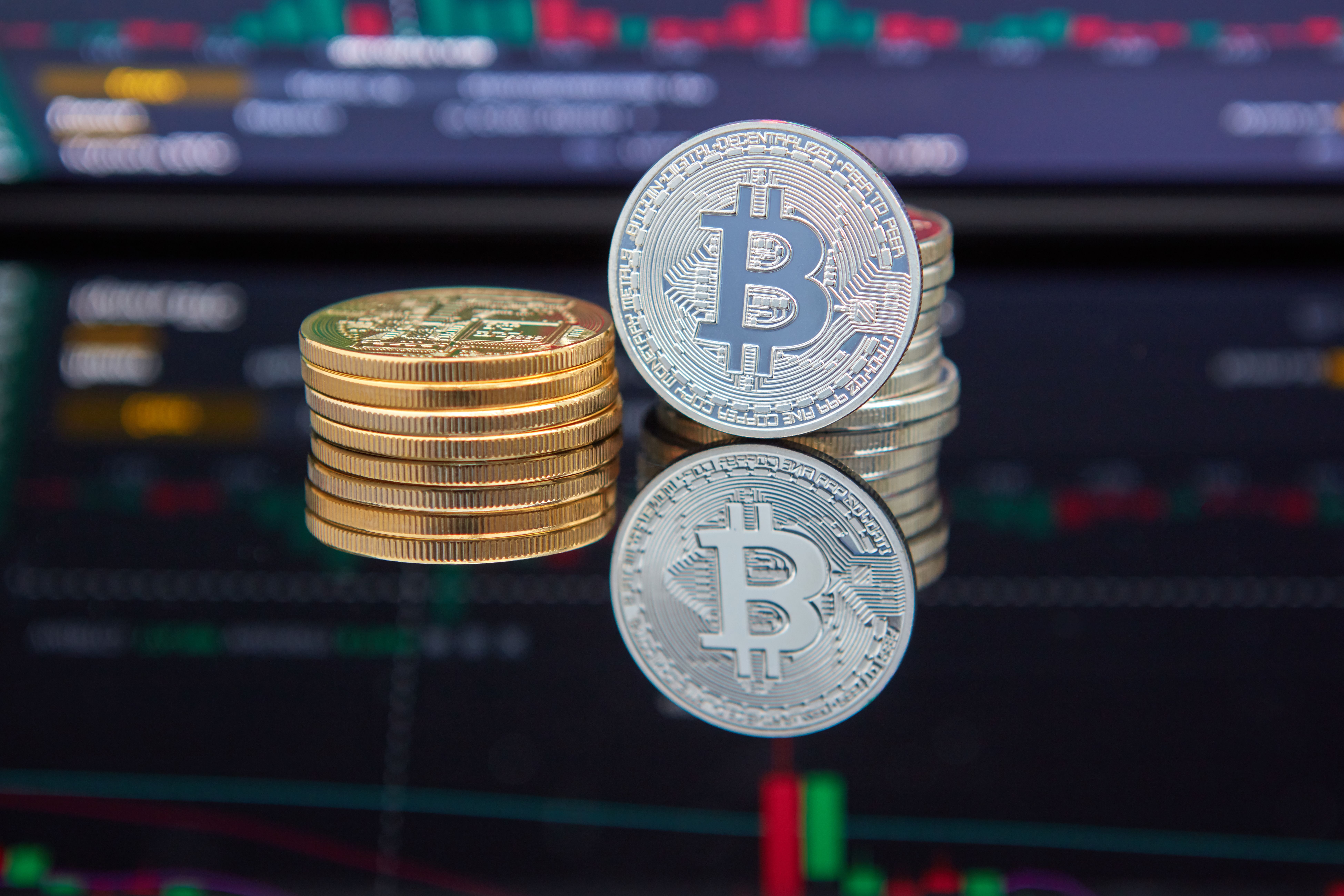 A close-up of a single physical bitcoin on a dark, monochrome surface, low monumental light