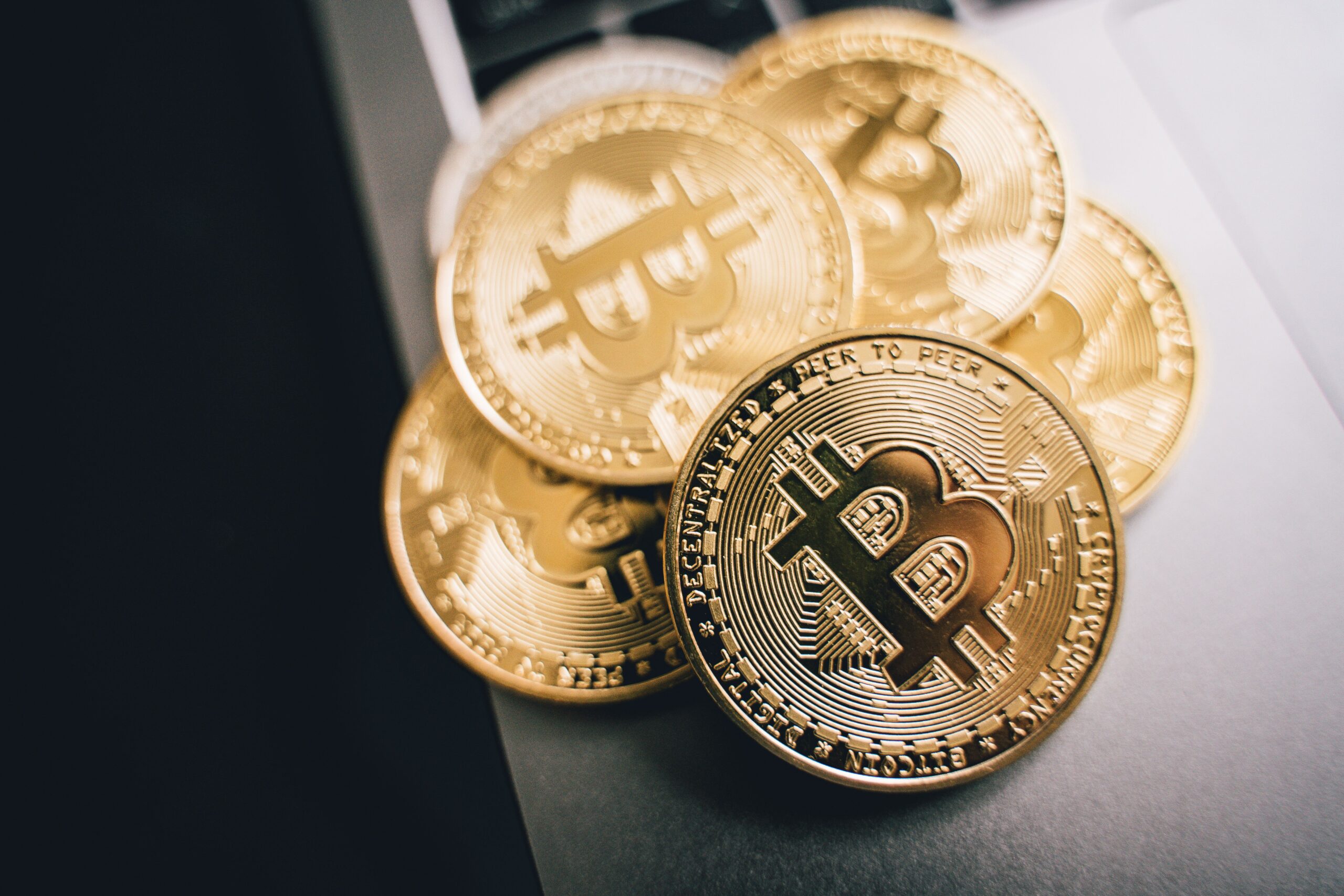 A single hand reaching toward a dark monochrome bitcoin coin under one light source